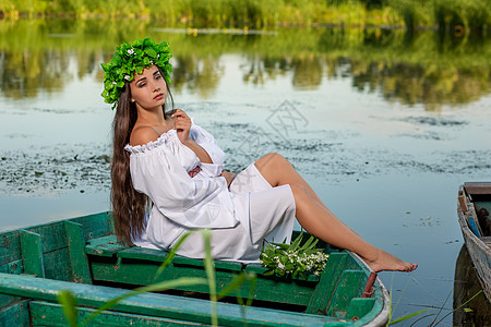 深色头发长发的女神 穿着白色古董礼服 坐在河中央的一条船上童话花朵裙子冒充女孩神话魅力海滩成人美人鱼图片