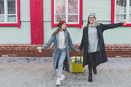秋季或春季 两名快乐的旅游女性微笑着提着手提箱在城市街道上行走  旅游和度假概念行李女孩咖啡建筑享受朋友们假期电话游客青少年图片