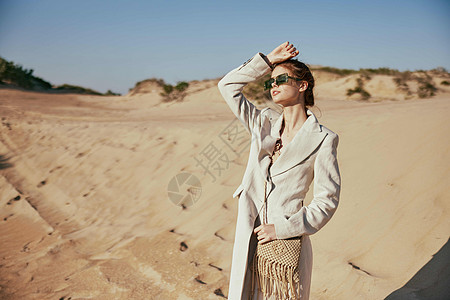 挎着包的女孩一位身穿轻便夹克和太阳镜 肩上挎着包的女性的水平肖像 在沙漠的背景下摆姿势天空太阳幸福沉思平衡女孩红发活力快乐呼吸背景