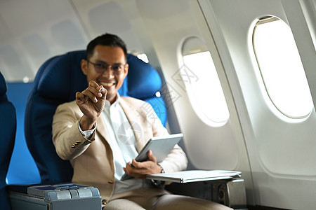 在商务旅行期间坐在机舱时使用数字平板牌 身着优雅豪华西装的笑笑脸商务人士照片图片