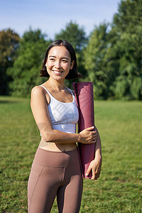 年轻亚洲健身女孩与橡胶垫子一起散步以做瑜伽的垂直肖像 继续公园新鲜空气培训 穿运动服等运动装成人福利运动赛跑者日落慢跑者跑步快乐图片