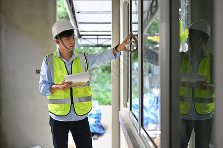 身戴安全头盔和防伪衣的亚洲男子视察员 手持剪贴板 视察重建后的建筑图片