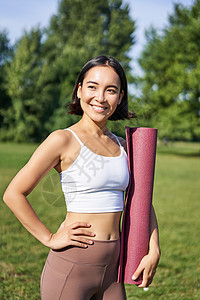 年轻亚洲健身女孩与橡胶垫子一起散步以做瑜伽的垂直肖像 继续公园新鲜空气培训 穿运动服等慢跑者运动员成人运动装女孩跑步运动日落福利图片