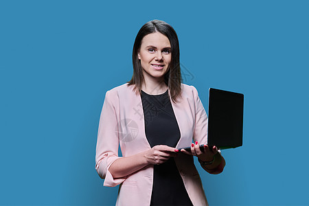 带着笔记本电脑 蓝背景的微笑的年轻商业妇女肖像人士老师教练金融网络培训师职业夹克成人律师图片