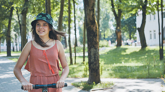 夏天在公园里骑着电动摩托车的女孩的肖像女士微笑女性运动鞋运动活力闲暇街道技术自行车图片