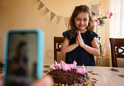 穿着海军礼服的漂亮生日女孩 握起手掌 许个愿 在节日蛋糕上吹蜡烛前图片