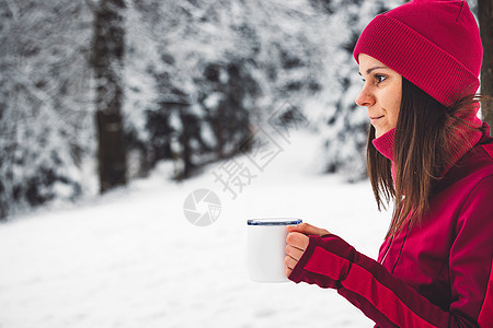 侧面情况 腰部上身 穿红色夹克和帽子的女人 在寒雪的冬季森林中喝热茶女性微笑假期快乐喜悦毛衣云杉雪花乐趣女孩图片