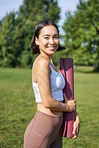 带着橡胶垫微笑的健身女孩 站在公园里穿着制服参加锻炼和体育活动 在草坪上做户外瑜伽太阳运动员运动训练工作赛跑者成人慢跑者跑步日落图片