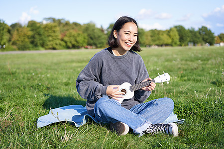 棕褐发女孩快乐 学生在公园的草地上玩木偶游戏 放松 歌唱 生活方式概念歌曲音乐家吉他幸福成人乐器弦琴唱歌女性乐趣图片