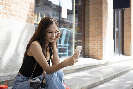 坐在城外的户外时 有智能电话视频的亚洲女性开心起来图片
