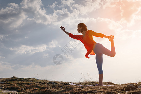 女人以姿势做瑜伽 站在山上石头上的一块地毯上 在云和太阳的阴影下闲暇平衡瑜珈活力运动训练女性成人锻炼身体图片