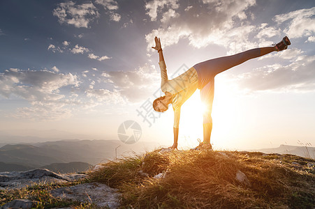 做运动的人女人以姿势做瑜伽 站在山上石头上的一块地毯上 在云和太阳的阴影下闲暇平衡成人运动瑜珈身体女性训练活力锻炼背景