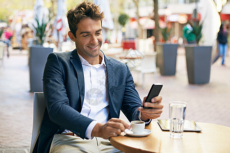 一位年轻商务人士在户外咖啡馆喝咖啡时使用手机 (他用手机打听了电话)图片