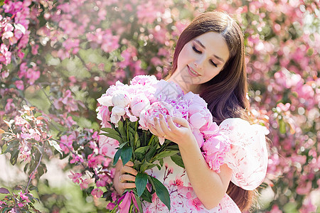 一个穿着洋装的快乐黑发美女 带着一束巨大的花朵 站在粉红开花的苹果树附近花束舞蹈女孩运动裙子香气花园女士花瓣香水图片