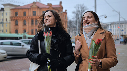 两个穿着夹克和外套的快乐朋友 带着郁金香在城里走来走去女孩们动作幸福友谊微笑女性人群成人冷天乐趣图片