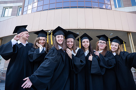 毕业学士在大学背景下 毕业礼服学生们在一连串地站着欢乐女士仪式教育庆典成人学校朋友们资质血统女性背景