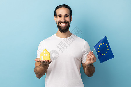 拿着欧盟旗帜和纸房子的人 梦想着在欧洲国家购买住宿图片