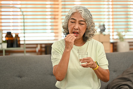 中年妇女拿着一杯淡水和取药的中年妇女 老年人保健 医药概念;以及图片