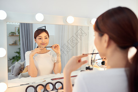 美丽的女人坐在镜子前 拿着刷子修妆的美貌女郎图片