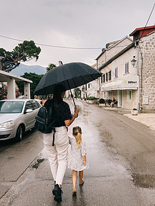 妈妈和一个小女孩 带着一只牵手的雨伞在街上走来走去图片