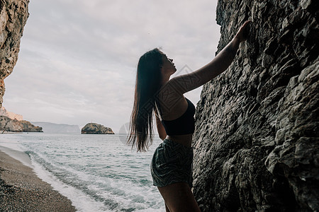 攀登岩石的体育妇女 身材苗条的年轻女子在火山玄武岩洞穴中攀爬 欣赏美丽的海景 女运动员在大自然中训练 女人克服困难的攀登路线力量图片