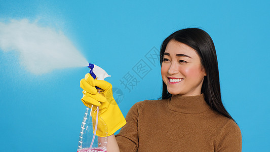 家庭清洁期间持喷雾器和粉尘机时身戴黄色橡胶橡胶手套的女管家图片