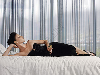 穿着优雅礼服的年轻女子 躺在床上喝着香槟杯图片