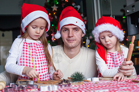 年轻爸爸有小女儿 在圣诞老人帽烤圣诞姜饼饼干 做圣诞糕点图片