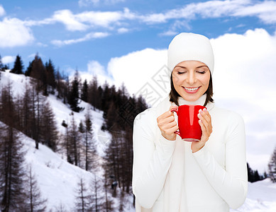 带着杯子的穿着冬衣 微笑着笑容的年轻女子 美丽的 阿尔卑斯山图片