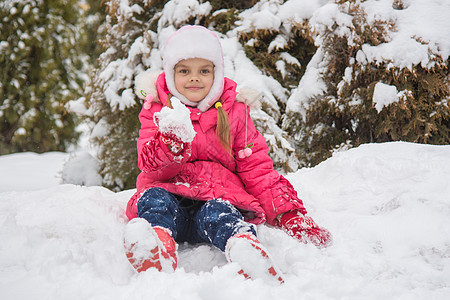 七岁女孩坐在雪中 雪让雪在他的手中保存着积雪图片