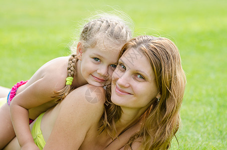 女儿躺在母亲背上 在绿草背景下 快乐地拥抱着她图片