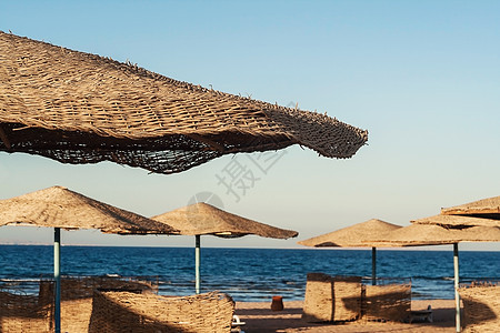 海滩上阳光明媚的一天 海滨背景的草伞雨伞 夏天 阳伞背景图片