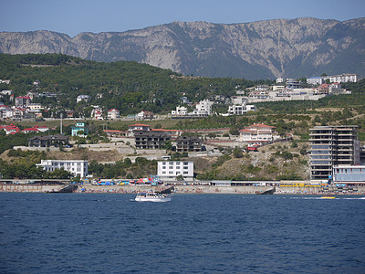 小船在海岸附近的海中航行 游客们在度假时可以在海岸上看到温泉小镇的房屋 背景是地平线上的高山图片