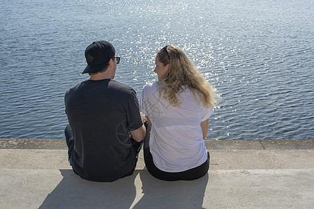 年轻夫妇坐在阳光下 在石码头看水亮水 太阳图片
