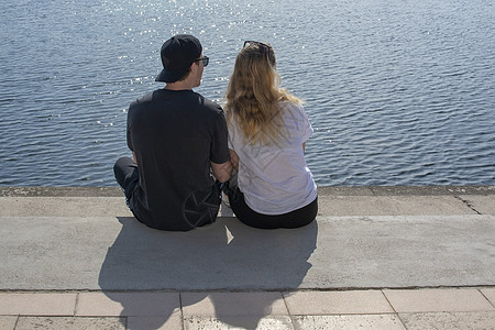 年轻夫妇坐在阳光下 在石码头看水亮水 喜悦图片