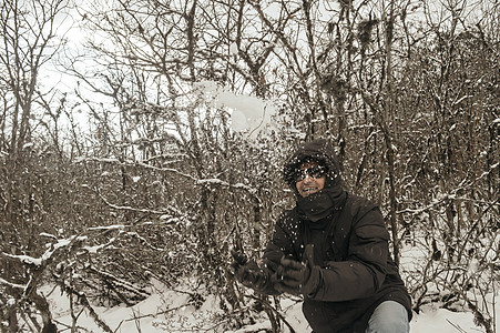 一个穿着黑色套头夹克的男人微笑着快乐地享受着第一场雪的玩耍和向空中扔雪球的肖像 在冬天享受下雪天的景色 农村查谟和克什米尔 图片