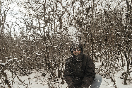 一个穿着黑色套头夹克的男人微笑着快乐地享受着第一场雪的玩耍和向空中扔雪球的肖像 在冬天享受下雪天的景色 农村查谟和克什米尔 图片