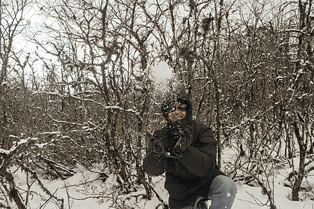 一个穿着黑色套头夹克的男人微笑着快乐地享受着第一场雪的玩耍和向空中扔雪球的肖像 在冬天享受下雪天的景色 农村查谟和克什米尔 图片