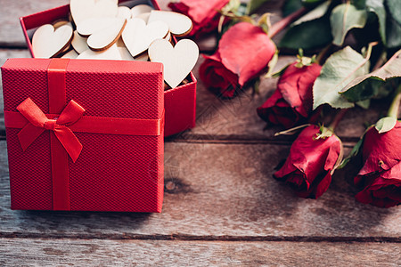 木制背景上的花玫瑰和红色礼品盒图片