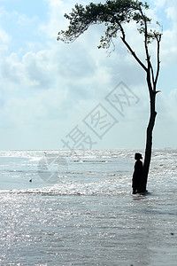 一个孤独的千禧一代单身女性站在远处的一棵树下 在蓝色海洋的海浪表面 晴天夏天海滩海岛 旅游旅游假期享受生活背景概念图片