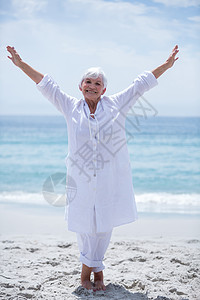 在海边伸展着双臂的 富足的老妇人图片