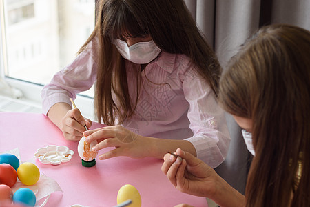 两名身戴医疗面罩的女孩在为复活节做准备时用刷子涂彩蛋图片