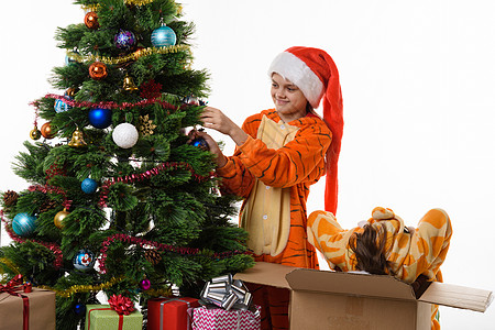 一个女孩把一个球挂在圣诞树上 另一个女孩带着头 爬进盒子里背景图片