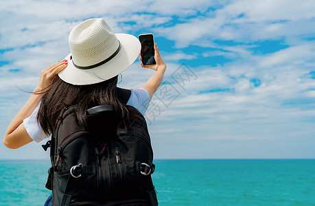 年轻的亚洲背背包妇女戴帽子使用智能手机自取 天空 天堂图片