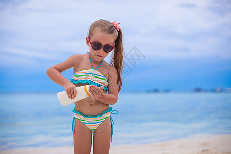 穿泳装的小女孩穿泳衣的可爱小女孩 拿着防晒霜水瓶子 棕褐色背景