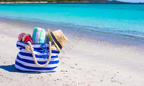 白沙滩上的蓝包 草帽 翻滚式拖鞋和毛巾 海洋图片