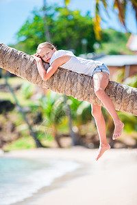 热带沙滩上可爱的小女孩 暑假时坐在棕榈树上图片