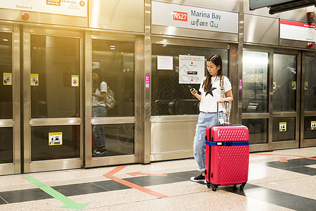 在新加坡Marina Bay车站使用智能手机的行李使用应用程序的年轻的年仅旅行者图片