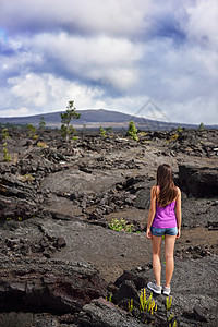 在美国夏威夷大岛火山的火山岩中徒步旅行的妇女 夏季旅游假期在火山黑岩上行走的旅游徒步者图片