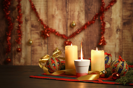 圣诞桌布上点着大火焰的蜡烛 周围有松树枝 剪纸小饰品 点燃的蜡烛和悬挂在木质背景上的圣诞装饰 具有散景效果 烛光 球图片